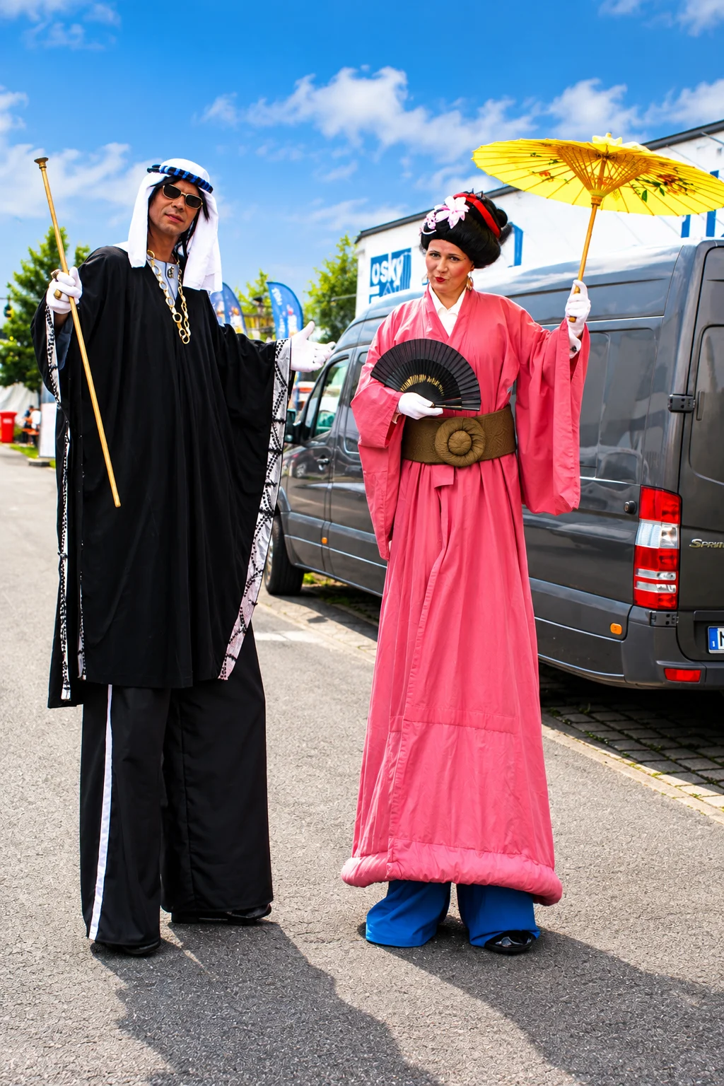 Stelzenkuenstler mit Faecher und Sonnenschirm